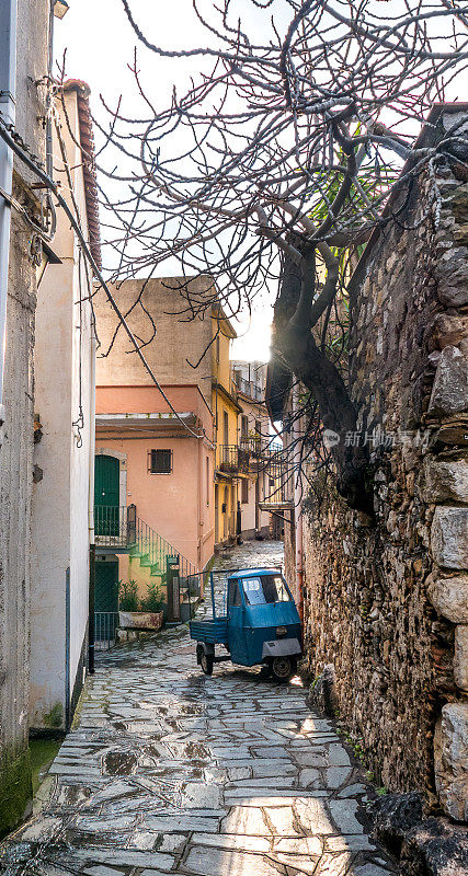 Castelmola,陶尔米纳,墨西拿。2017年3月:一辆涂着蓝色金属漆的传统老爷车，名叫Ape car，停在街上，旁边是一幢有大石墙的乡村房屋。